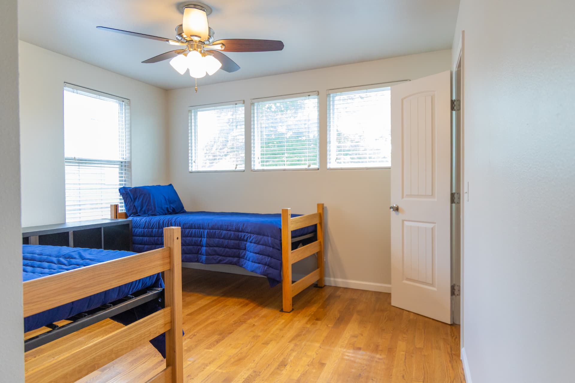 Corner bedroom with twin beds, ceiling fan, and a bank of windows