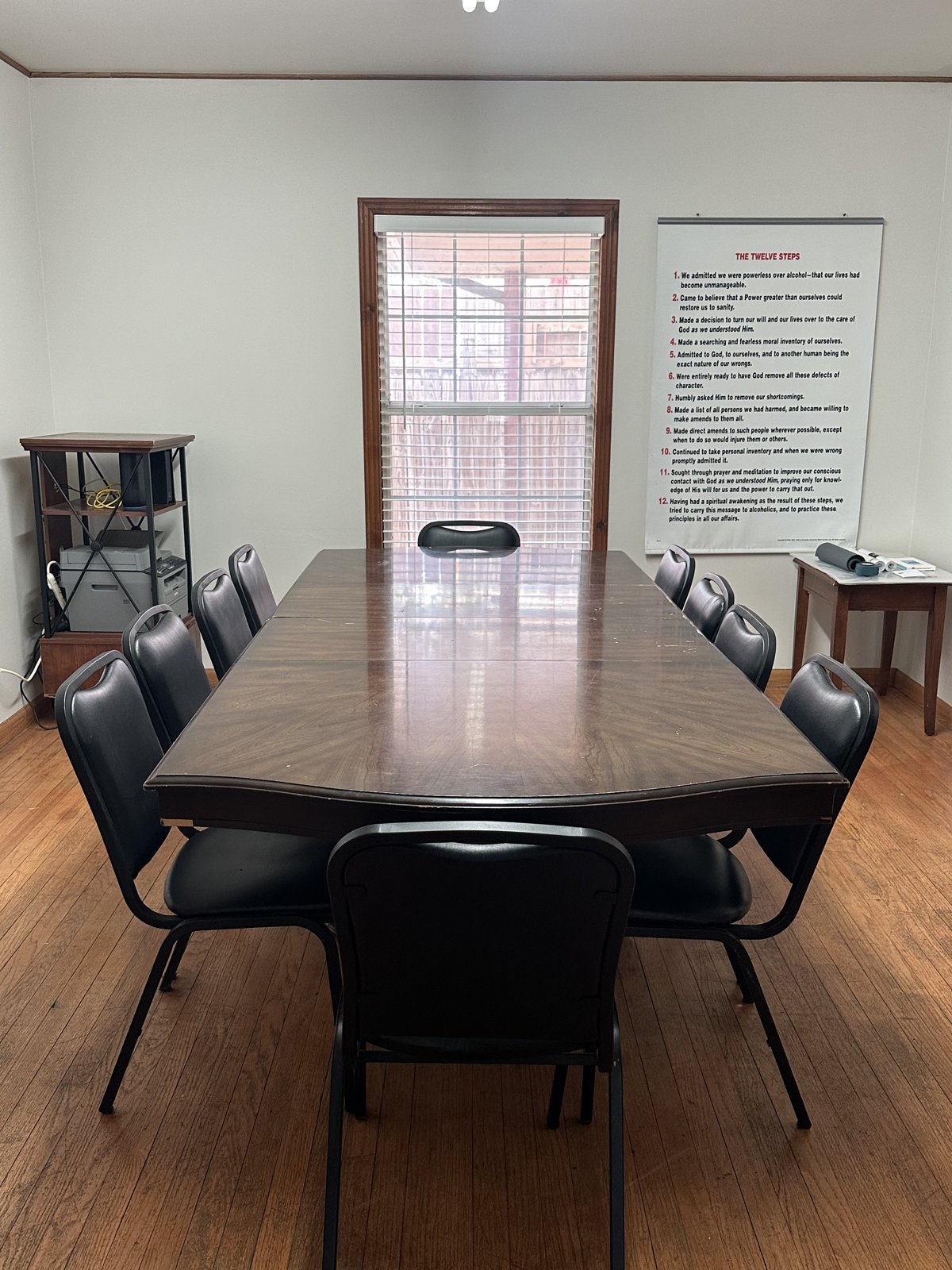 Meeting room with a long table, chairs, and the Twelve Steps on the wall